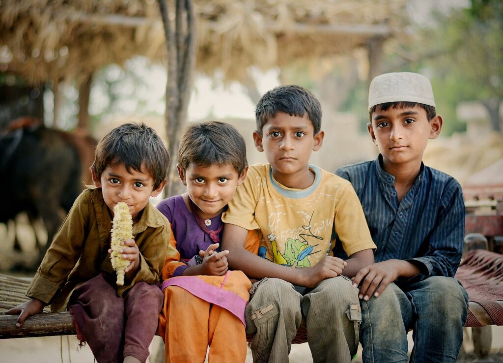 four children sitting on brown charpai bed