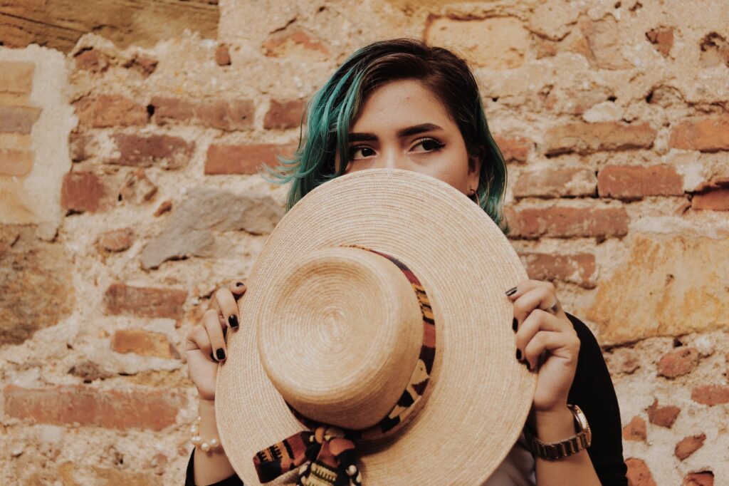 photo of woman covering her face with brown sun hat standing in front of brick wall