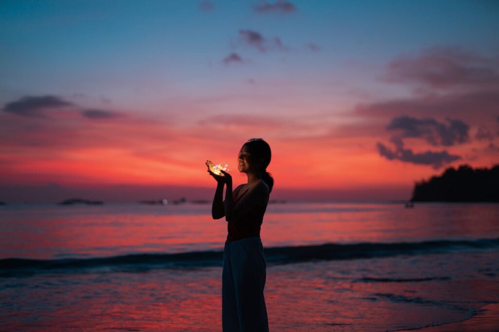woman holding lights on seashore at sunset