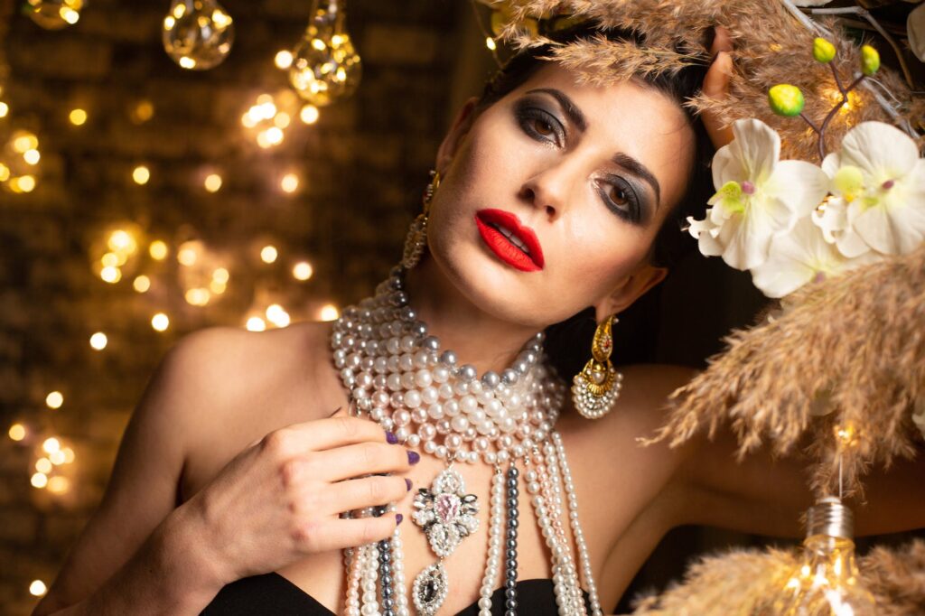 woman with bright makeup in pearl necklace looking at camera against garlands