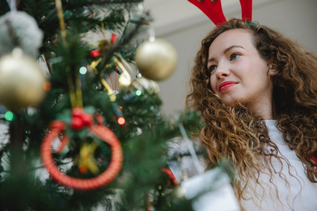 young woman decorating christmas tree with baubles